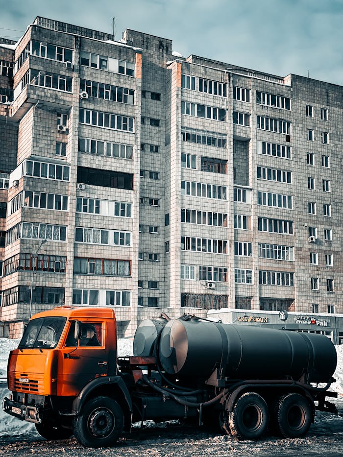 Orange industrial truck parked in front of a high-rise concrete building on a cold day.
